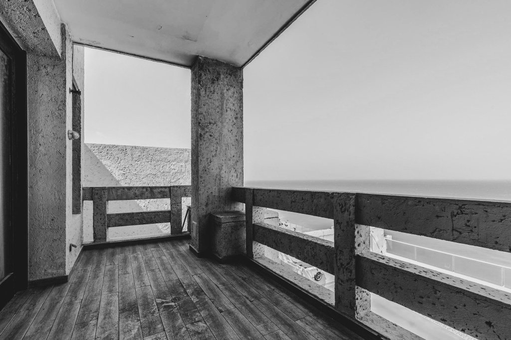 Balcón con vista al mar terminado en baranda de concreto, testigo inclemente de los cambios repentinos del entorno caribeño.